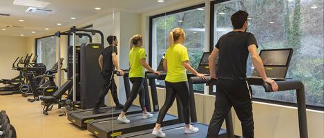 A gym with treadmills, weight machines, and a large window with a view of trees.