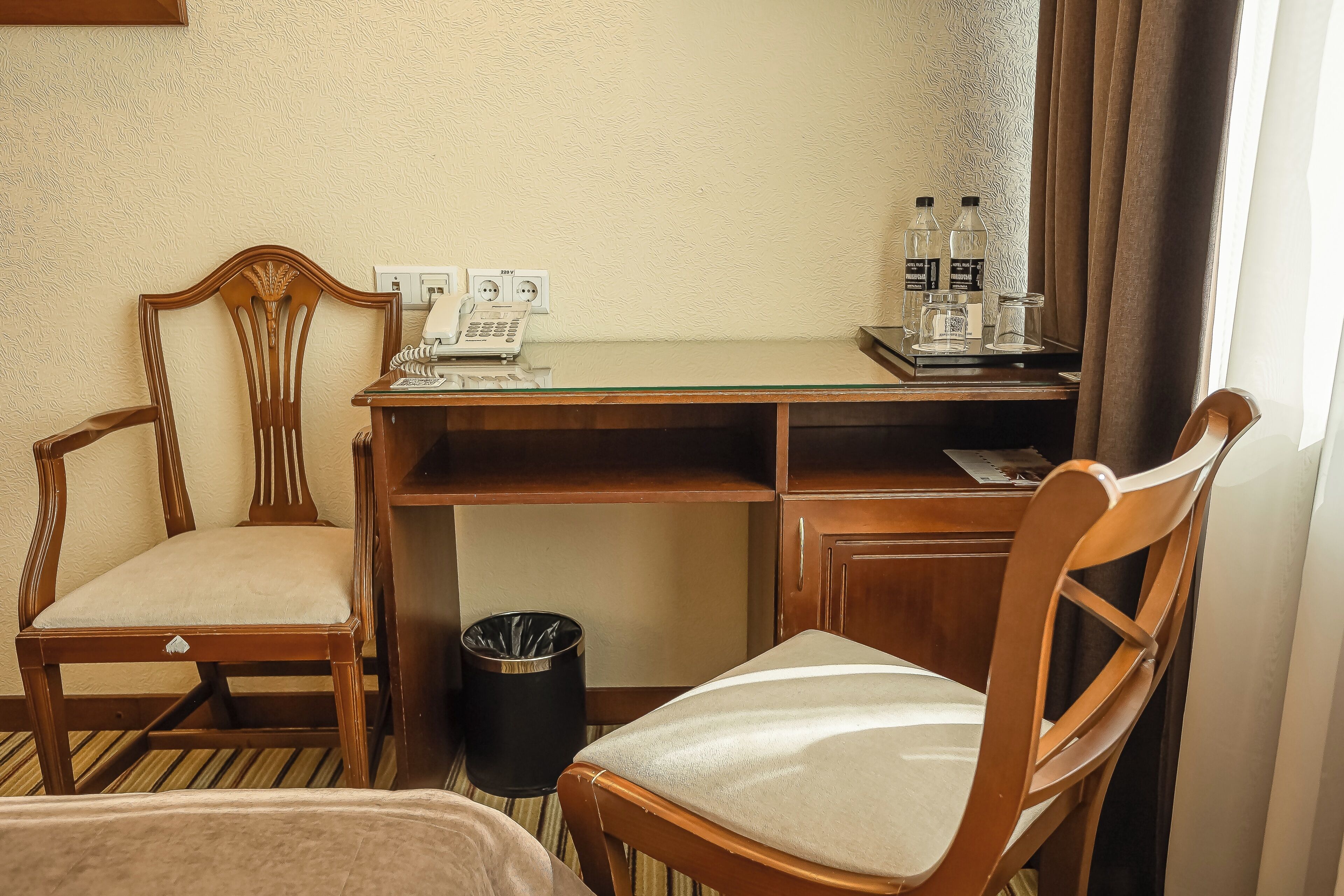 Ein Hotelzimmer mit einem Holztisch, zwei Stühlen, einem Mülleimer und einer Minibar.