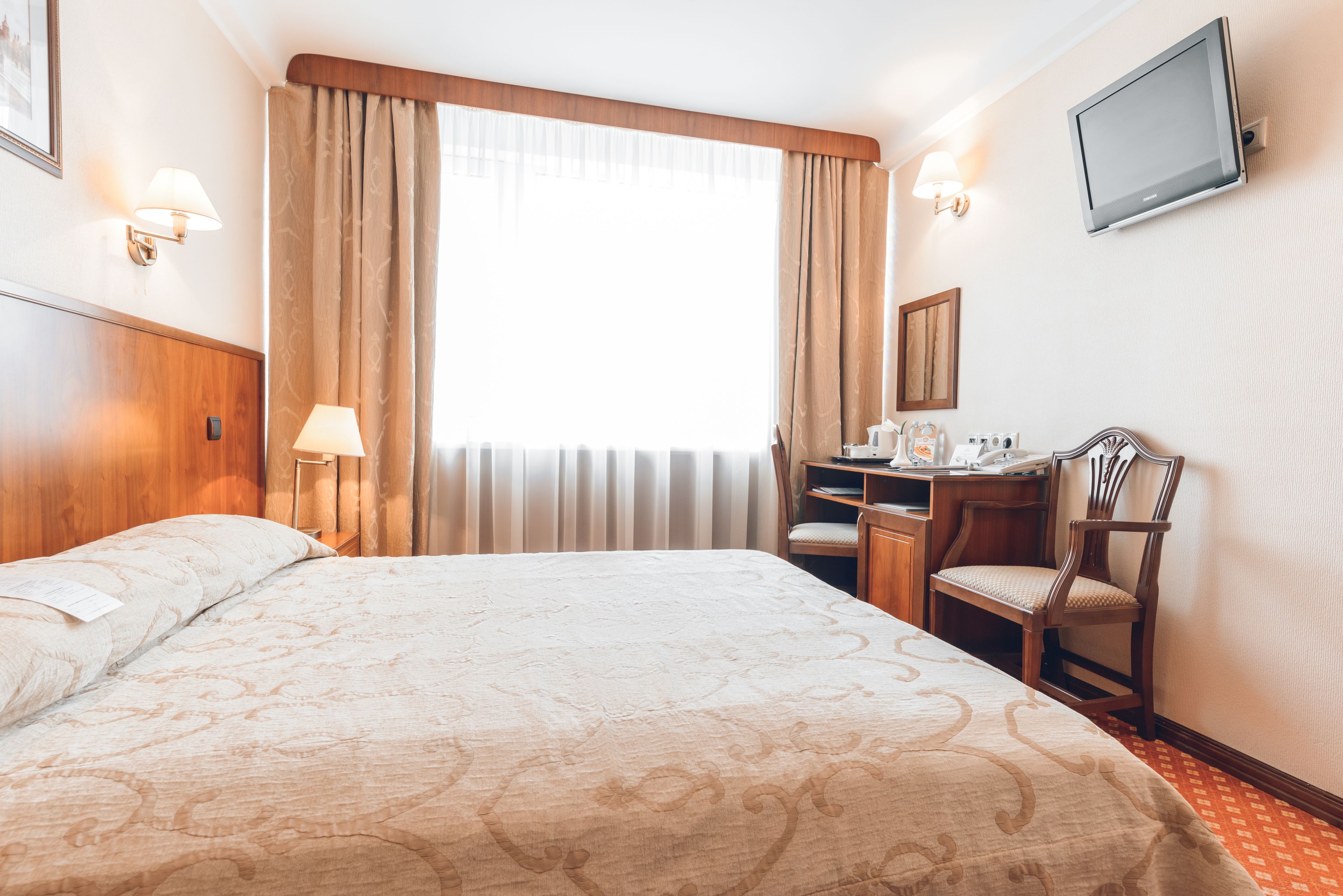 Una habitación de hotel con una cama grande, un escritorio con silla, televisión y ventana con cortinas.