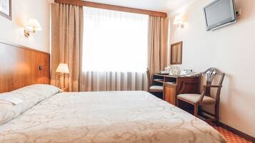 Una habitación de hotel con una cama grande, un escritorio con silla, televisión y ventana con cortinas.