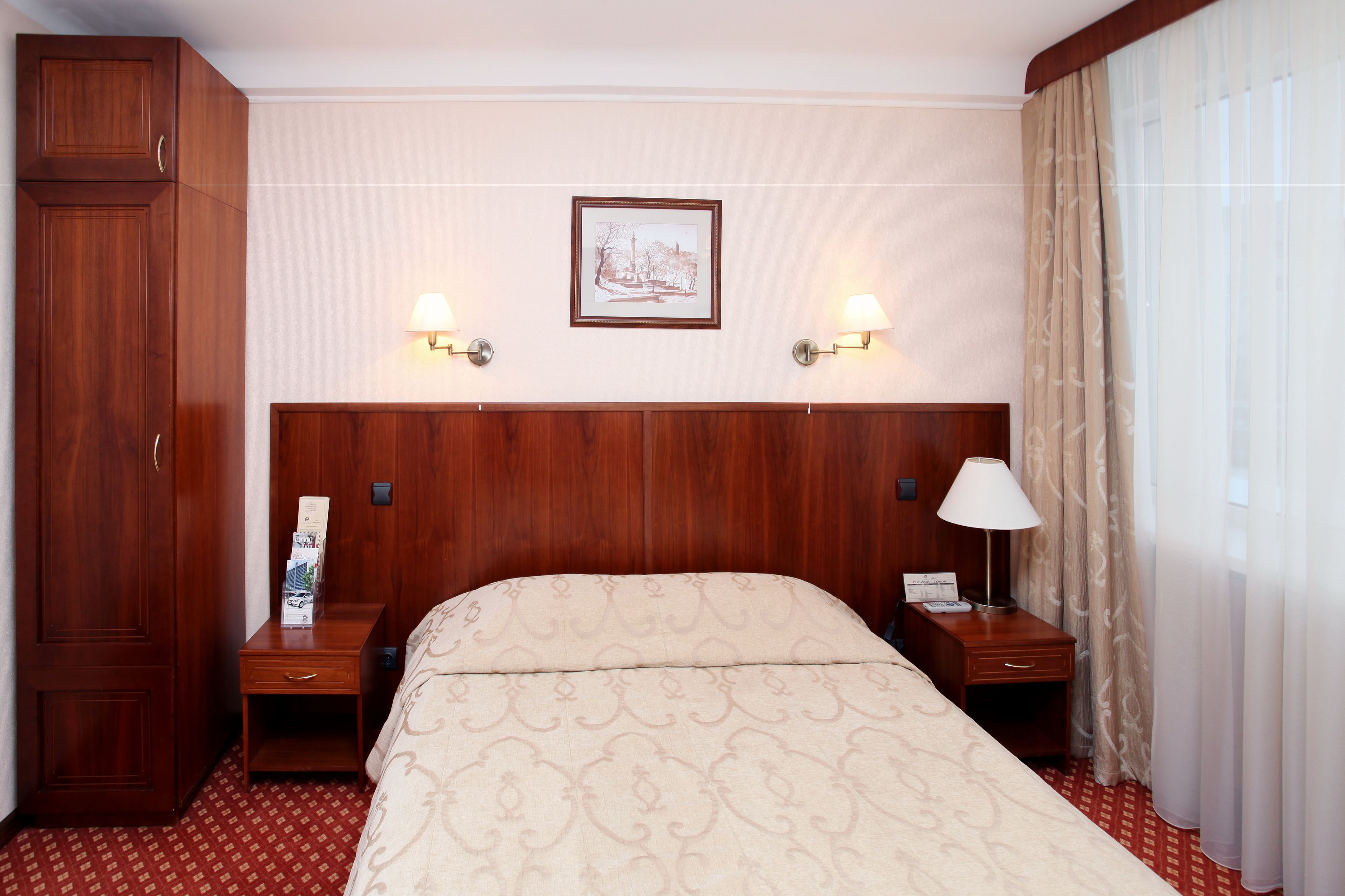 Une chambre d’hôtel avec un grand lit, une tête de lit en bois, deux tables de chevet avec des lampes, une armoire et un tableau encadré au mur.