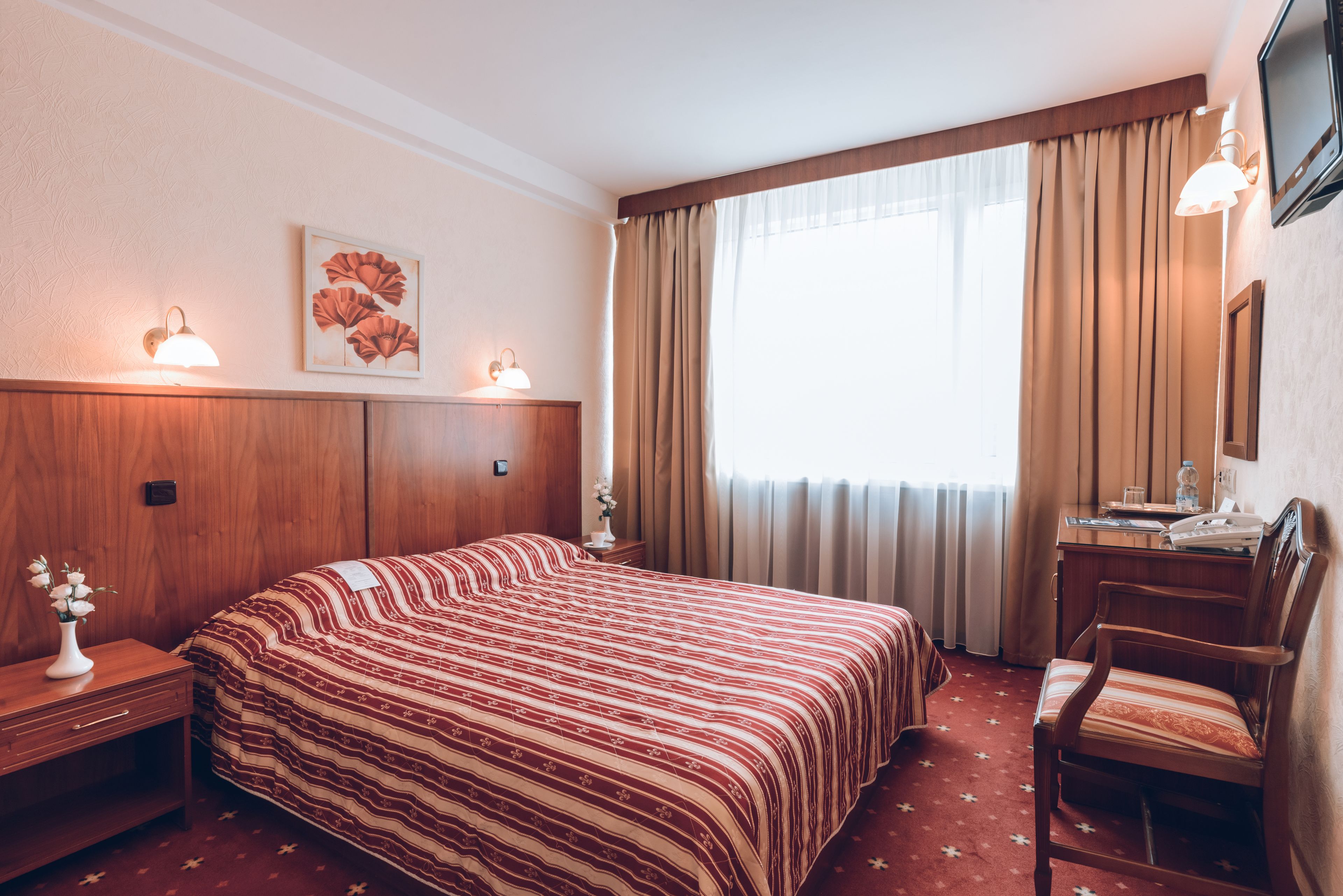 A hotel room with a large bed, a desk, a chair, a TV, and a window with curtains.