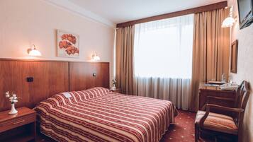A hotel room with a large bed, a desk, a chair, a TV, and a window with curtains.