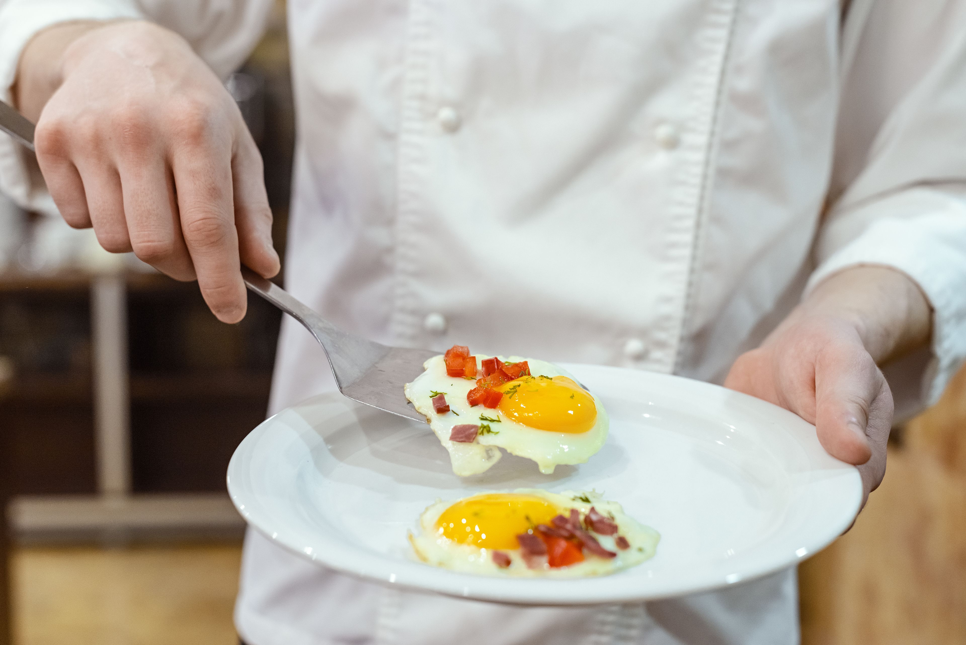 A chef holding a plate with two sunny-side-up eggs garnished with diced tomatoes and herbs.
