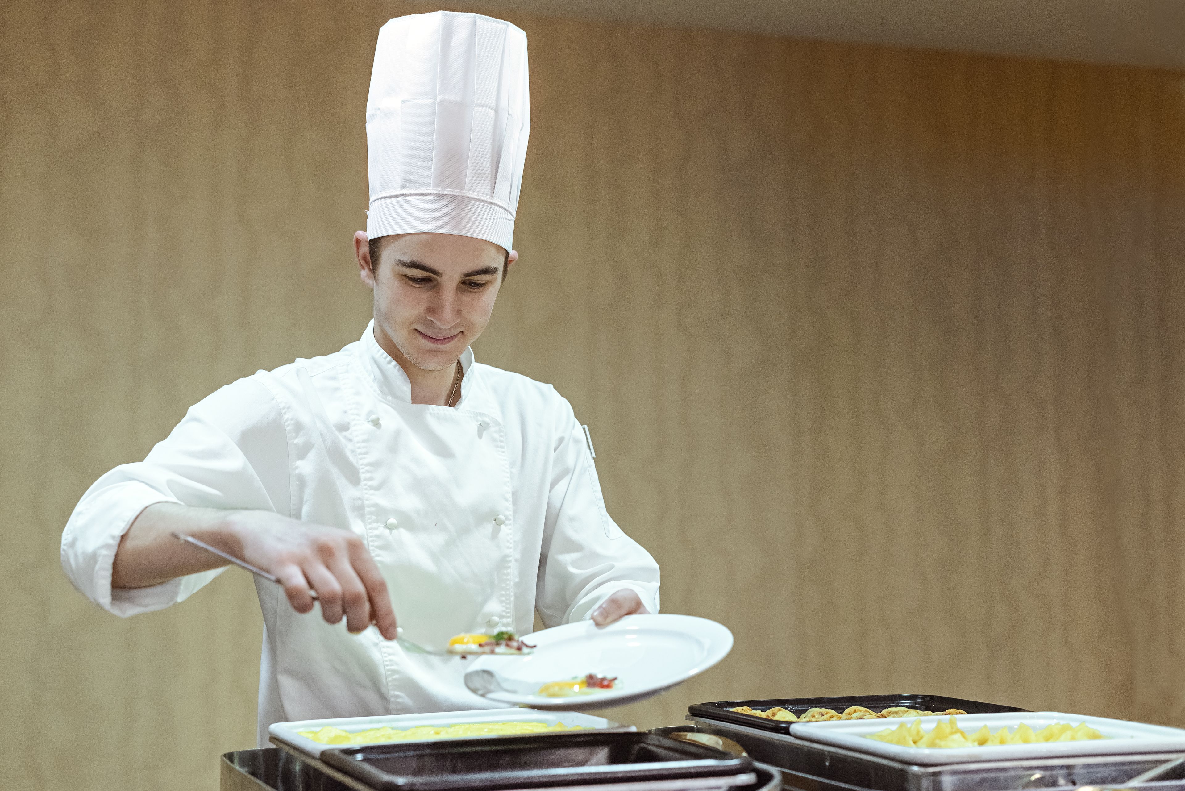 A chef in a white uniform and hat, serving food from a tray.