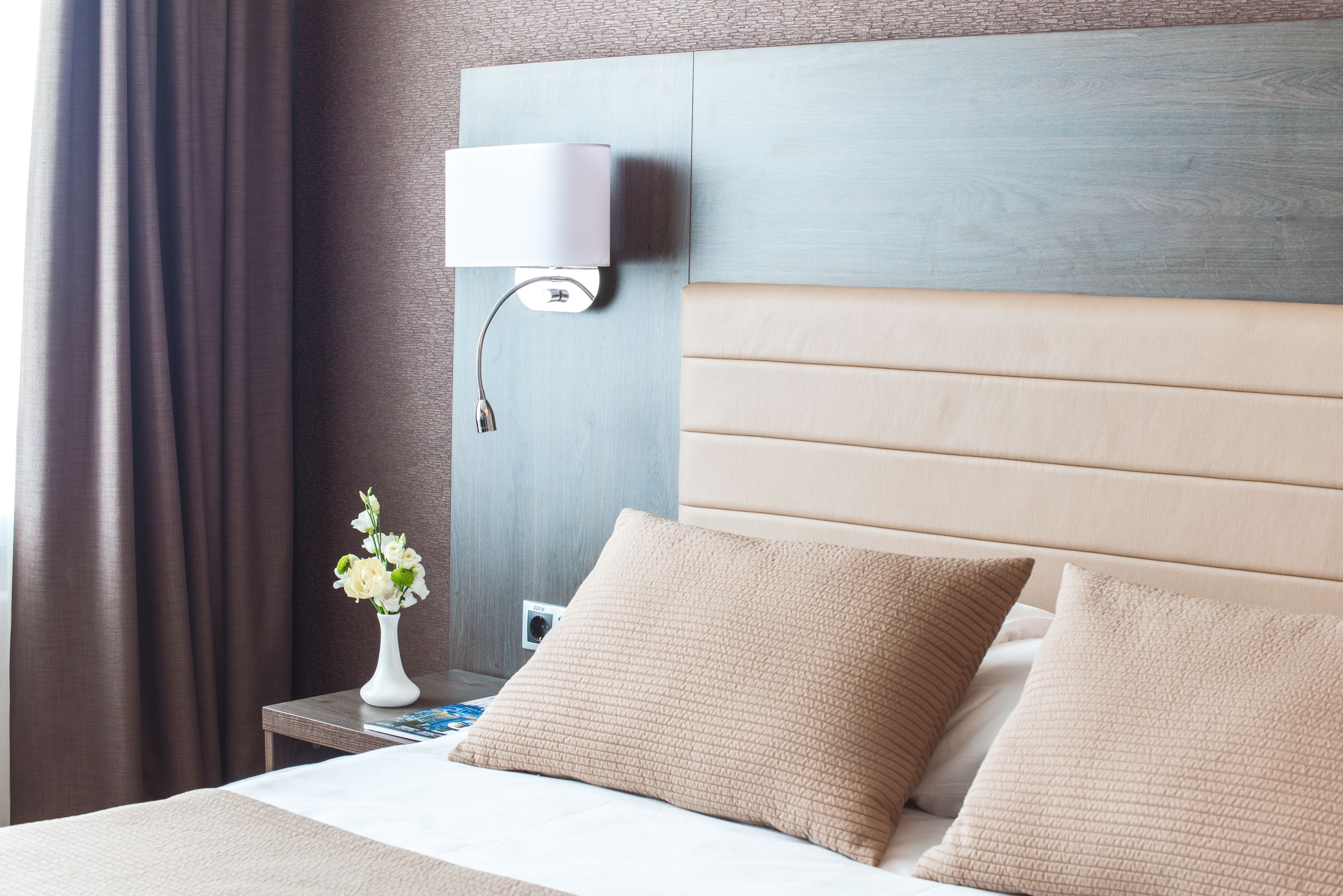 A hotel room with a bed, a nightstand, a lamp, and a vase with flowers.