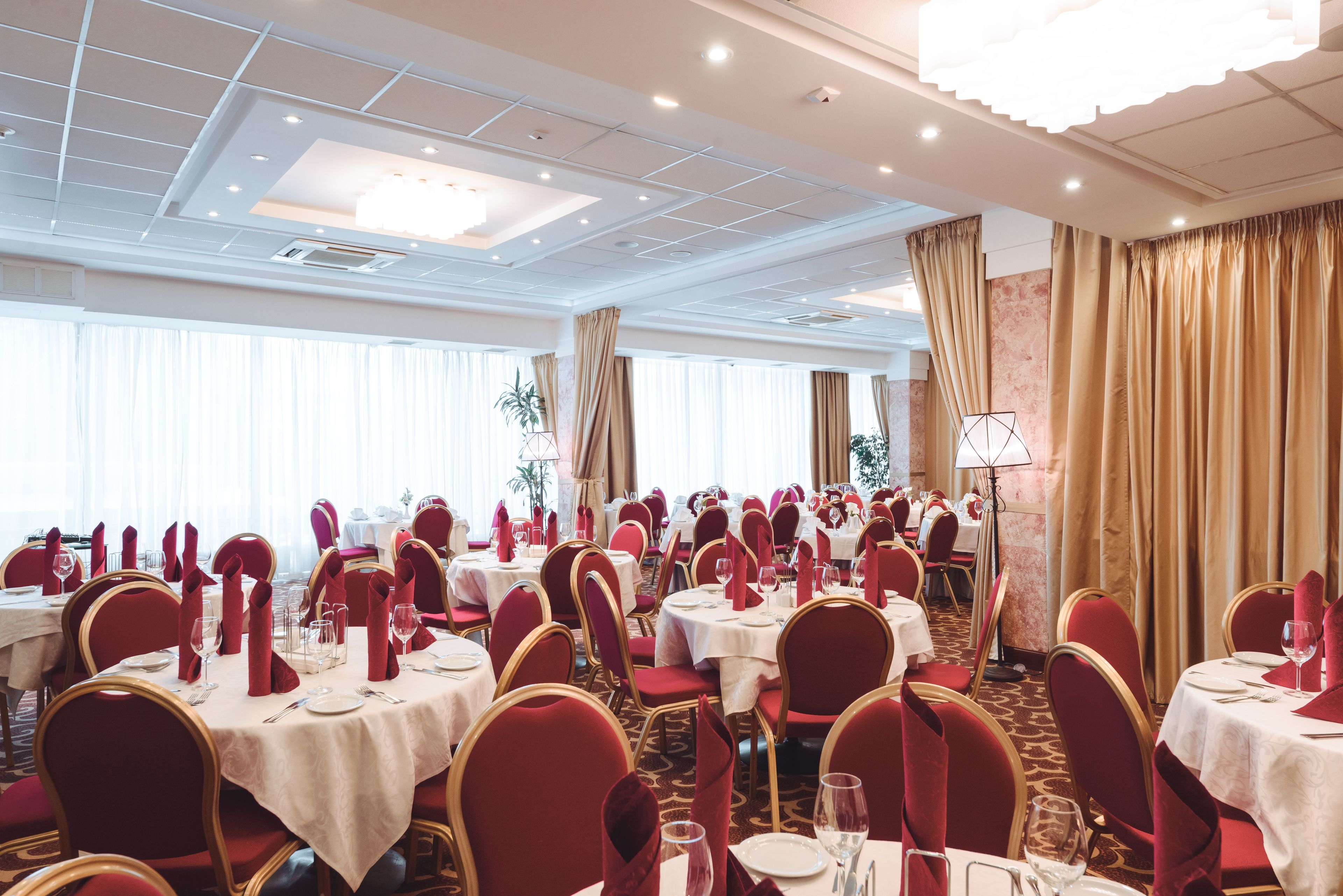 A banquet hall with round tables, red chairs, and white tablecloths.
