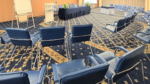 Une salle de conférence avec des rangées de chaises bleues, un tableau blanc, un pupitre et un écran de projection.