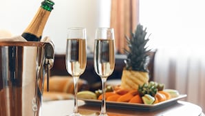 Une bouteille de champagne dans un seau métallique, deux coupes de champagne et une assiette de fruits sur une table.