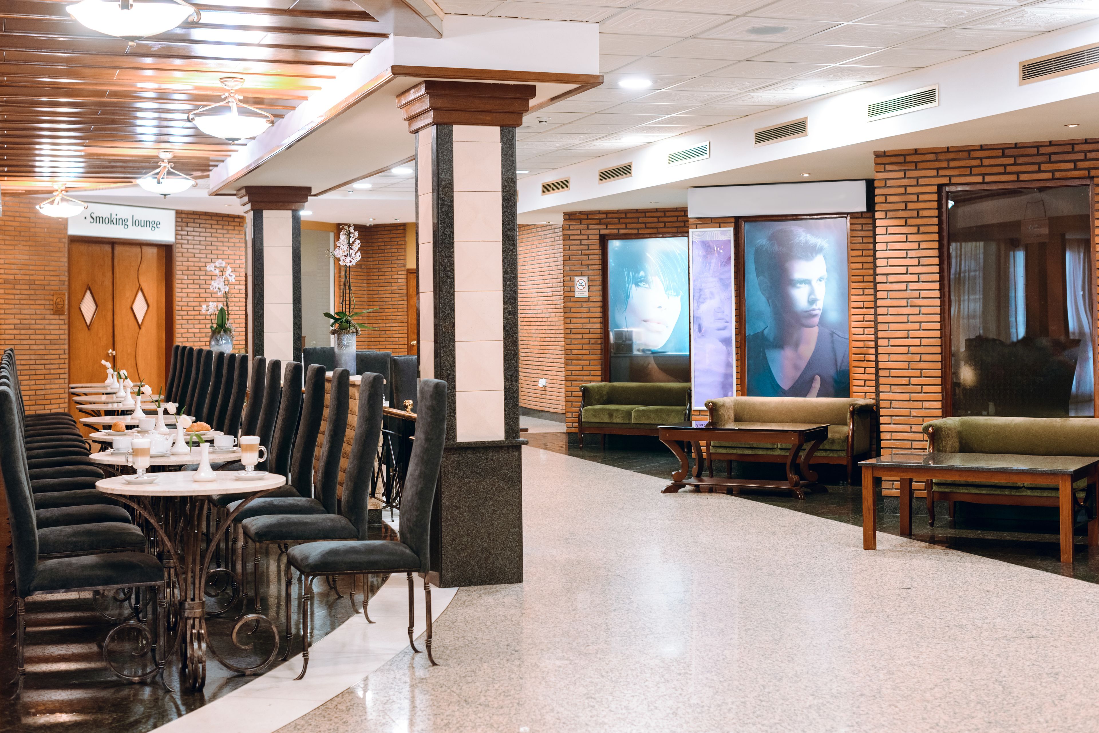 A restaurant with dark velvet chairs, round tables, and a brick wall with a large poster.
