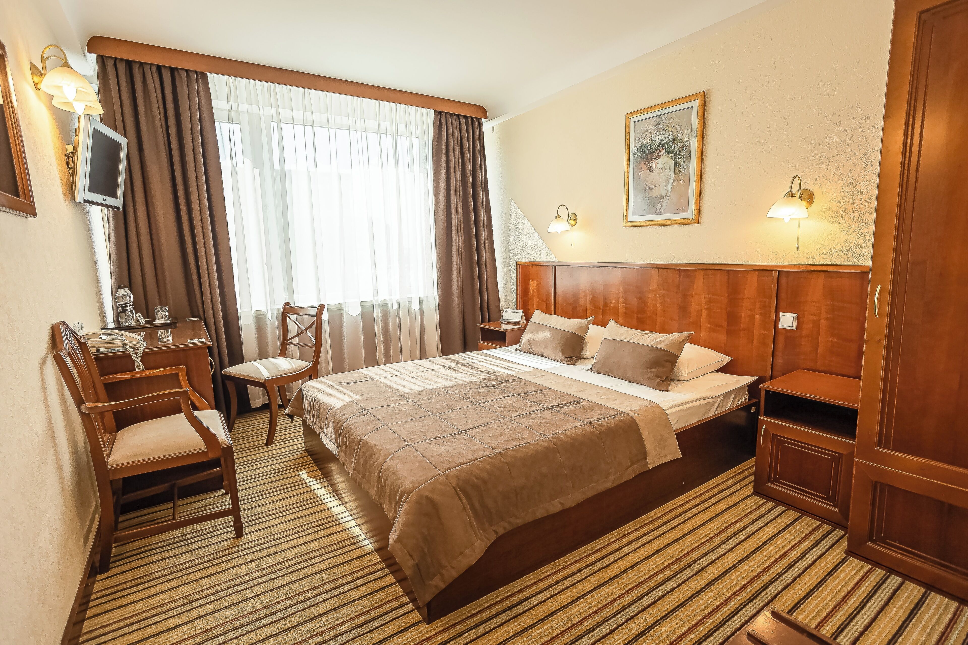 Habitación de hotel con cama, escritorio, silla, televisor y ventana con cortinas.