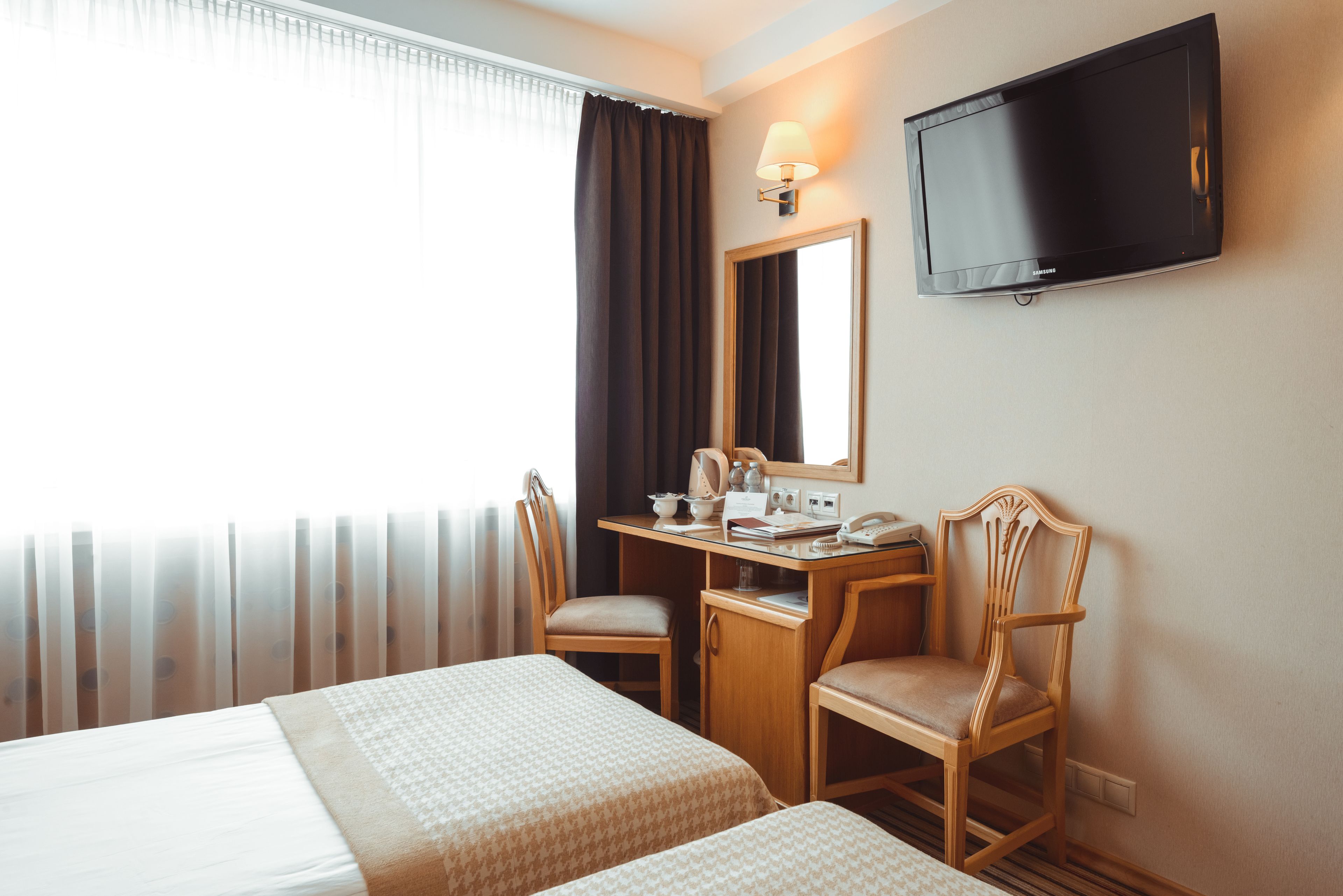 Habitación de hotel con dos camas, un escritorio con silla, televisor y ventana con cortinas.