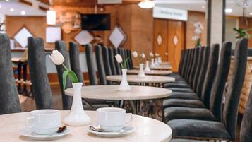 Een restaurant met ronde tafels en grijze, beklede zitbanken.