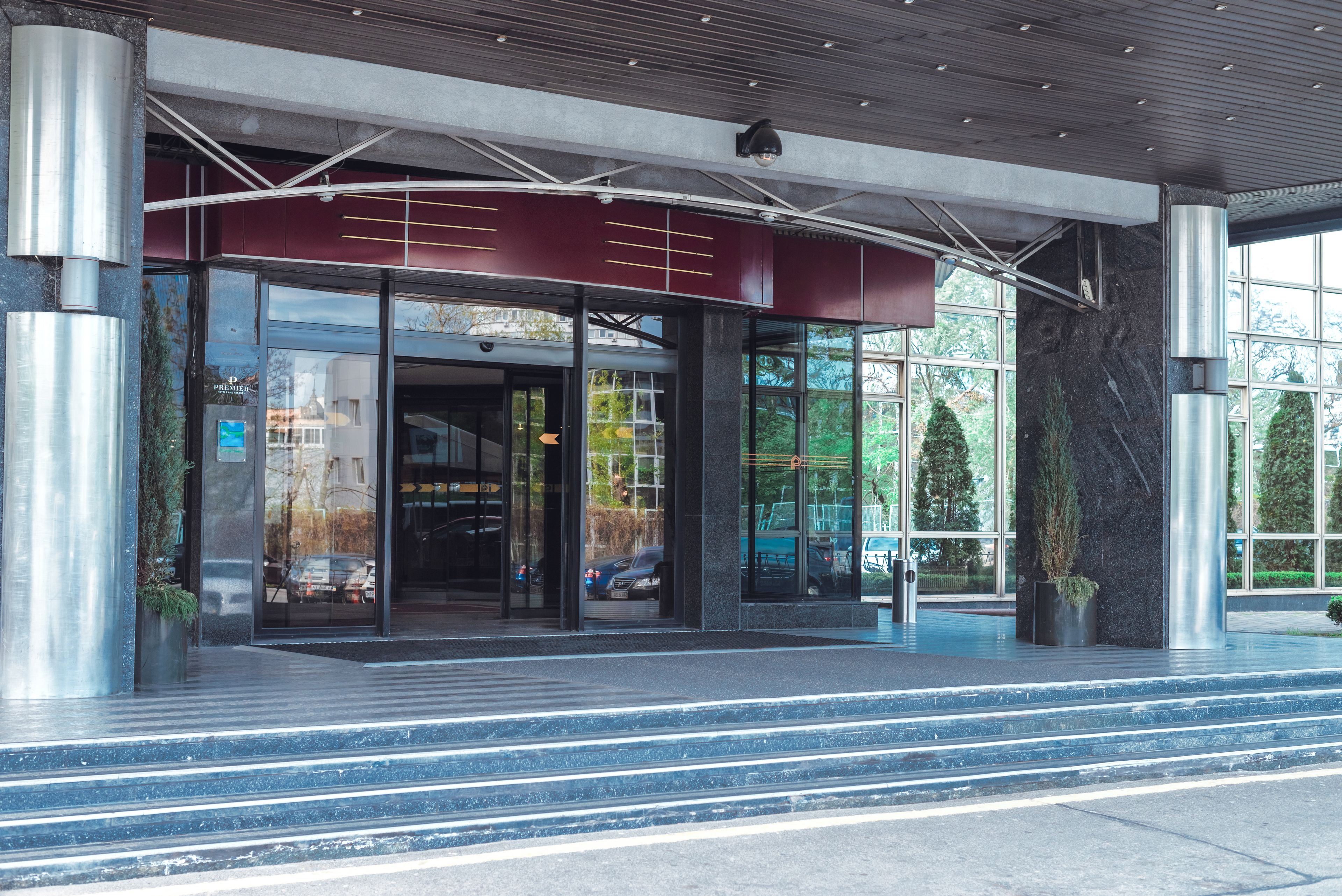 Una entrada moderna de edificio con puertas de vidrio, un toldo rojo y una escalera de metal que sube.