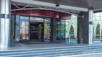 Una entrada moderna de edificio con puertas de vidrio, un toldo rojo y una escalera de metal que sube.