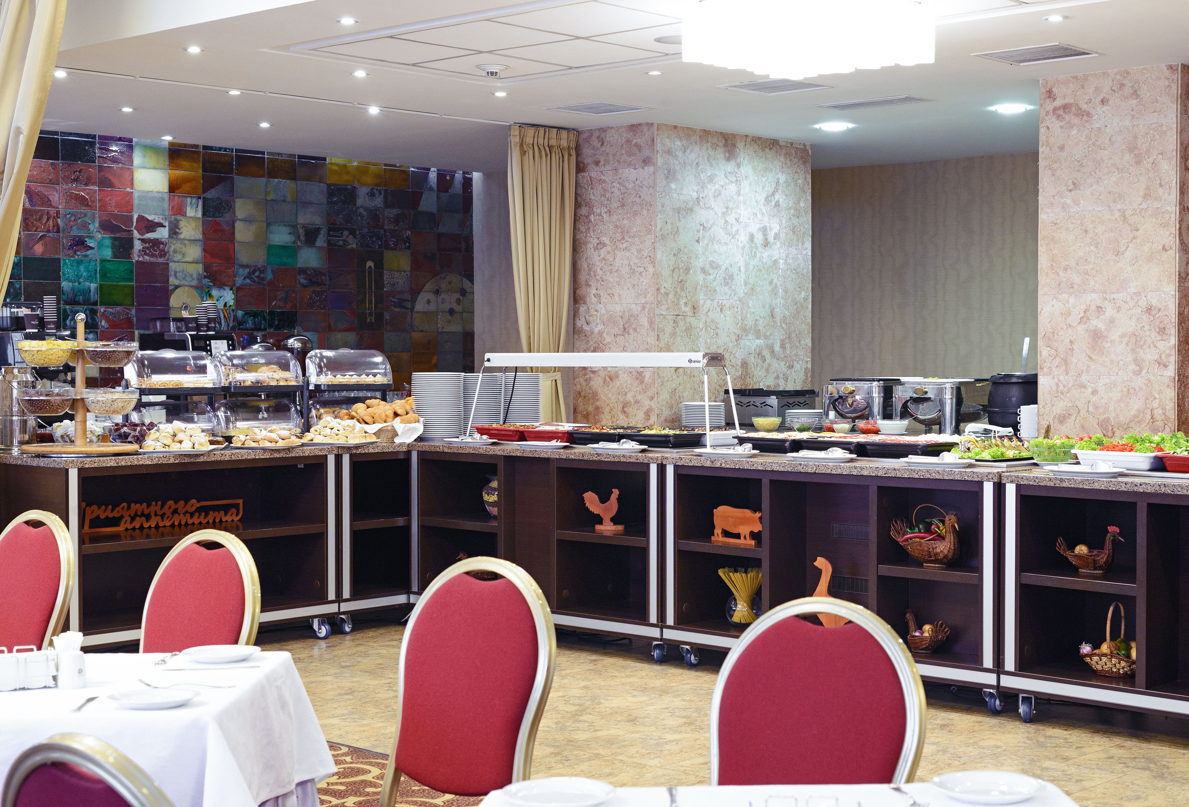 Un buffet garni de divers plats, un comptoir avec des appareils de cuisine et un mur recouvert de carreaux formant une mosaïque colorée.