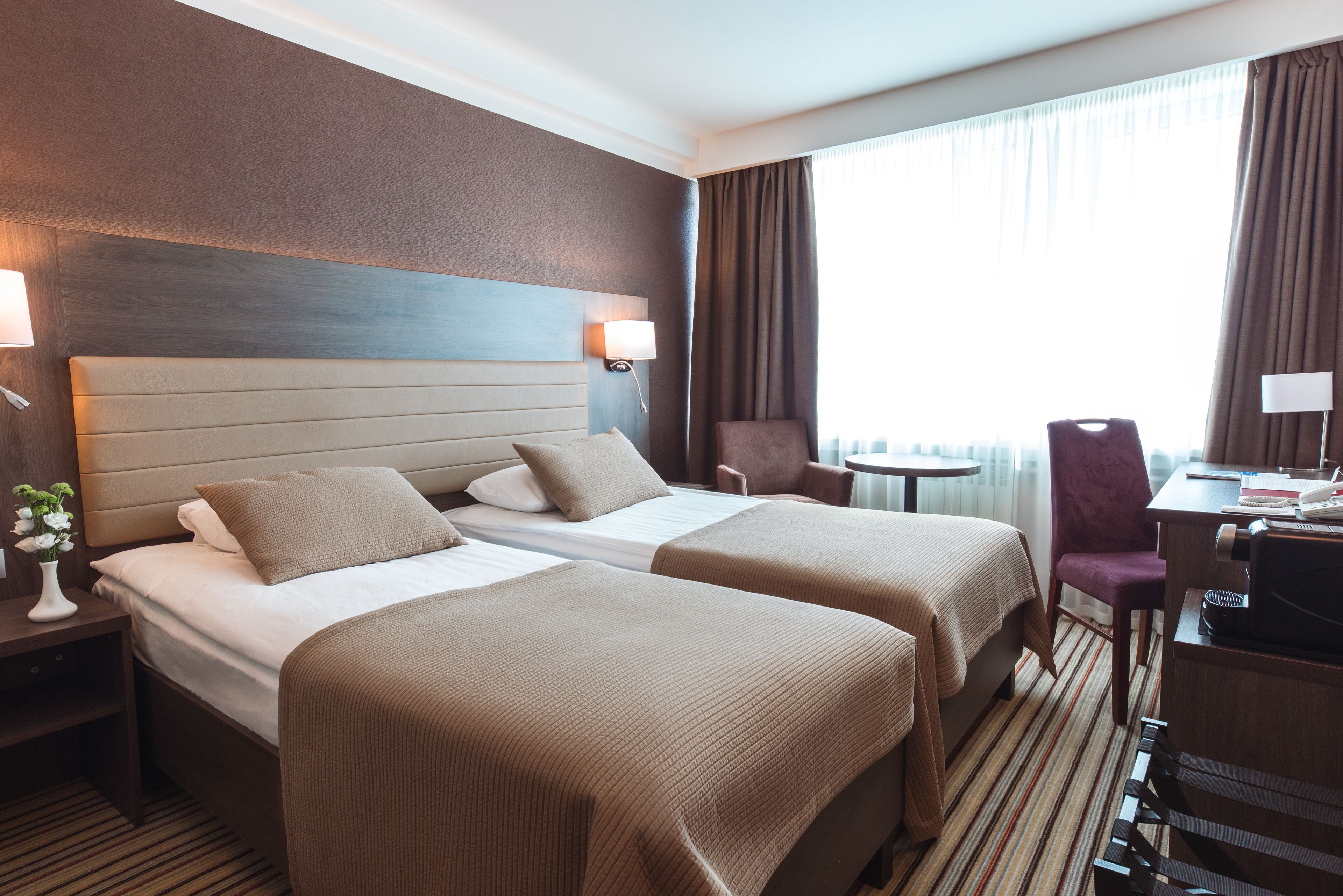 Une chambre d’hôtel avec deux lits, un bureau, une chaise et une fenêtre avec des rideaux.