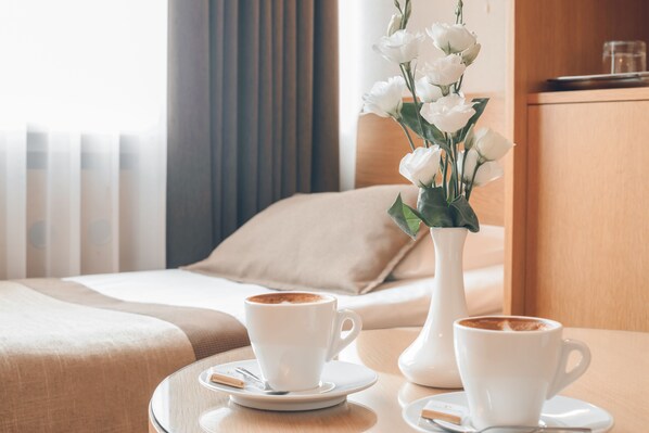 Une chambre d’hôtel avec un lit, deux tasses de café sur un plateau et un vase rempli de fleurs blanches.