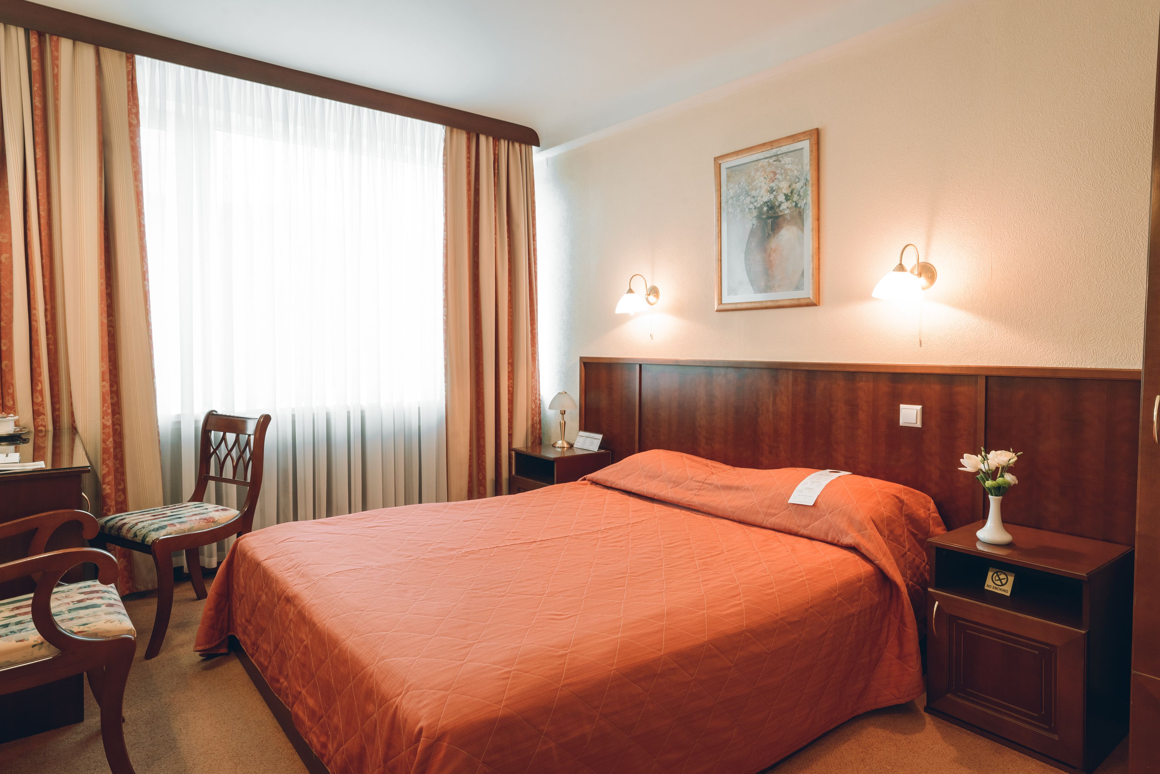 Une chambre d’hôtel avec un grand lit, un bureau avec une chaise, une table de chevet et un tableau au mur.