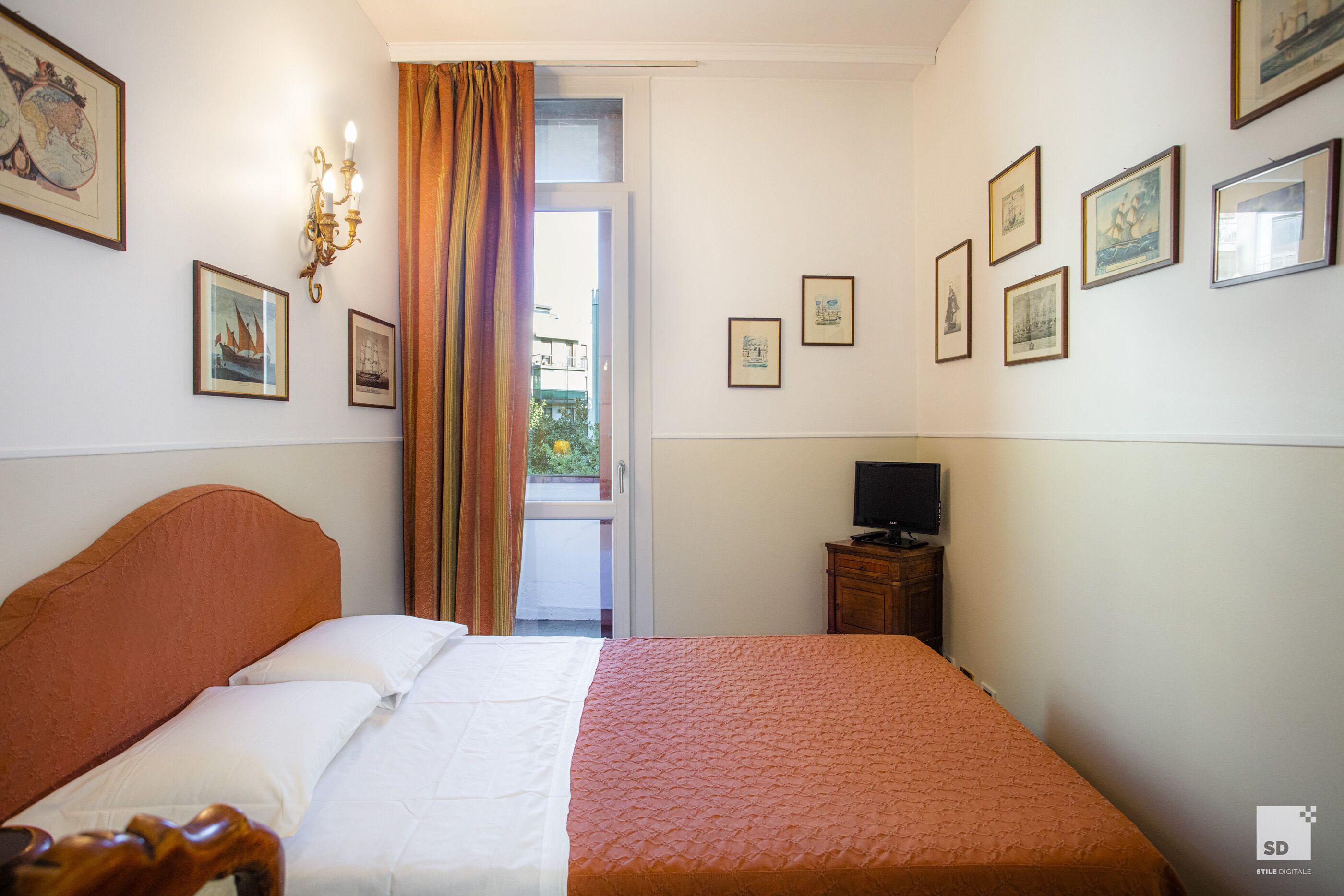 Una habitación de hotel con cama, televisión y ventana con cortinas.