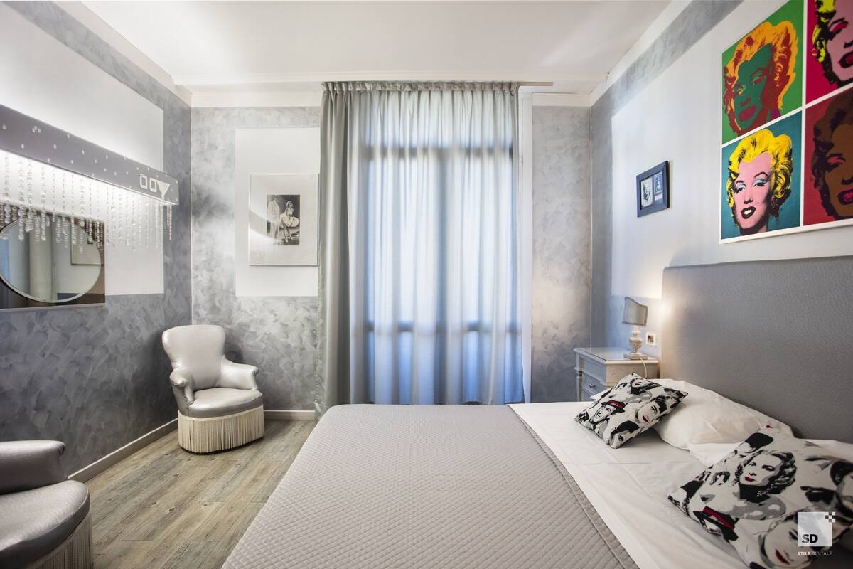 A modern bedroom with a large bed, a chair, a bedside table, and a mirror.