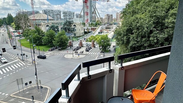 A balcony with two orange chairs and a black trash bin. A cityscape with buildings and a construction crane is visible in the background.