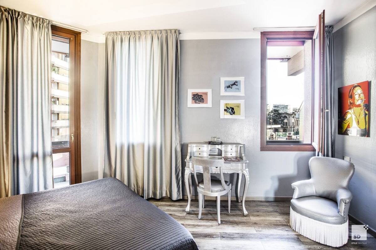 A hotel room with a bed, a desk, a chair, and a window with curtains.