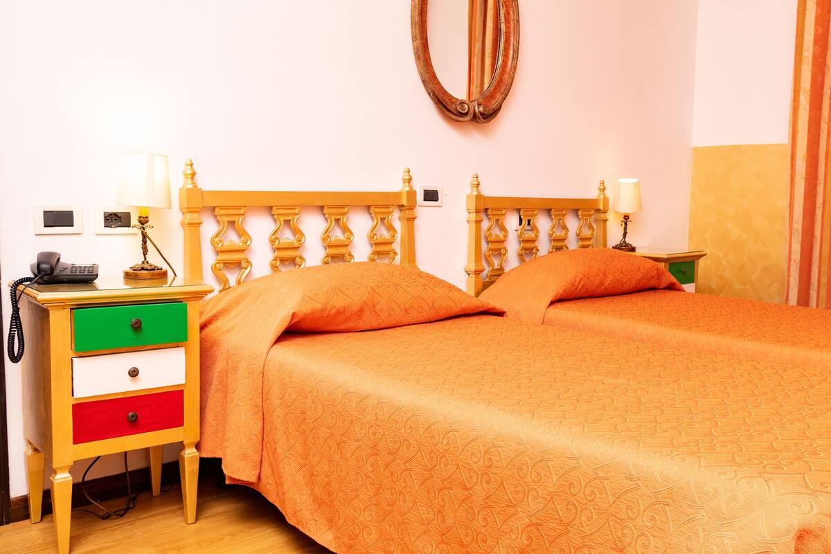A double bed with a wooden headboard, a bedside table with a lamp, and a green drawer unit.
