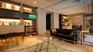 A modern living room with a sofa, a glass coffee table, and a bookshelf. - Hôtel Elixir (Paris)