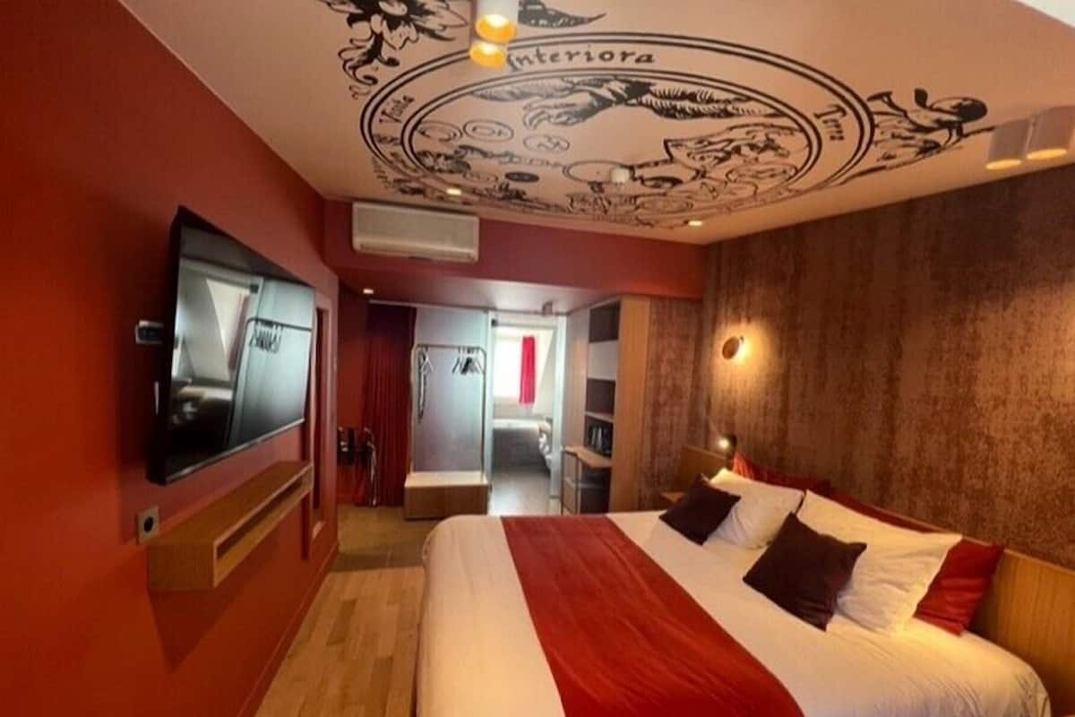 Ein Hotelzimmer mit einem großen Bett, einem an der Wand befestigten Fernseher und einer Decke mit dekorativem Muster.