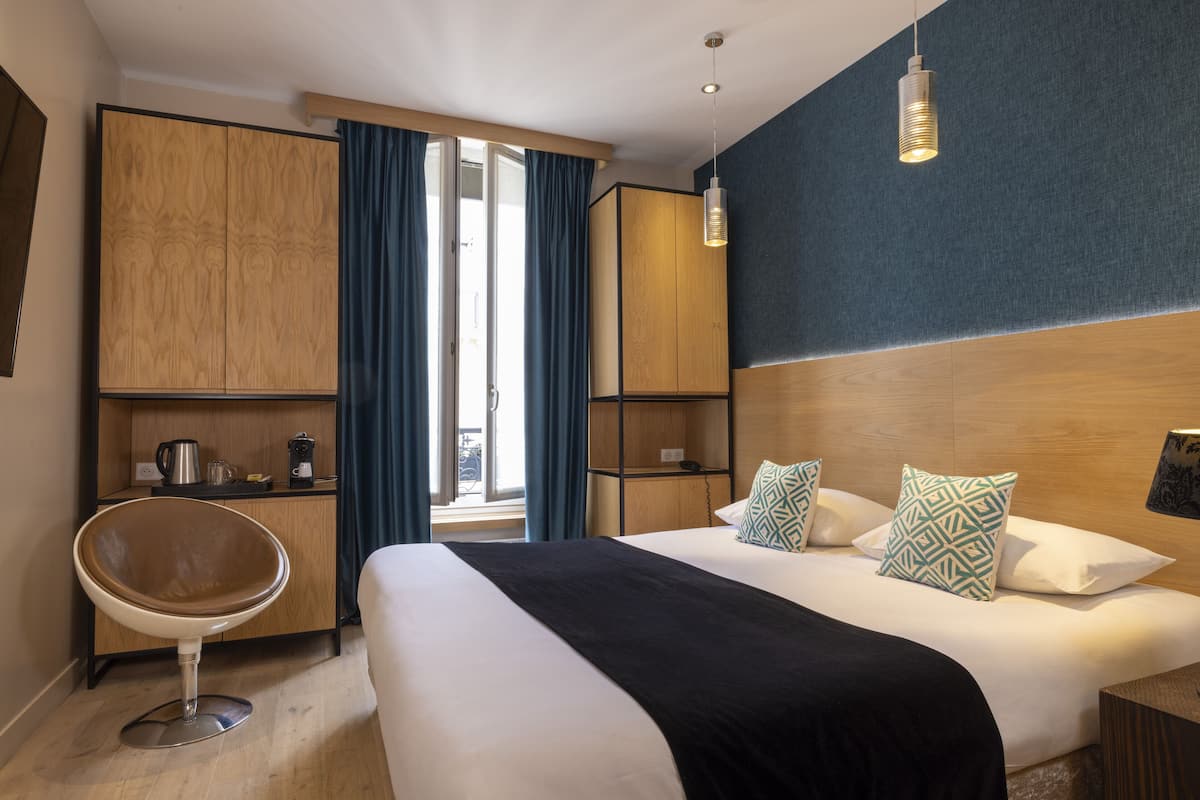 Ein Hotelzimmer mit einem Bett, einem Sessel, einem Schreibtisch und Blick ins Freie.