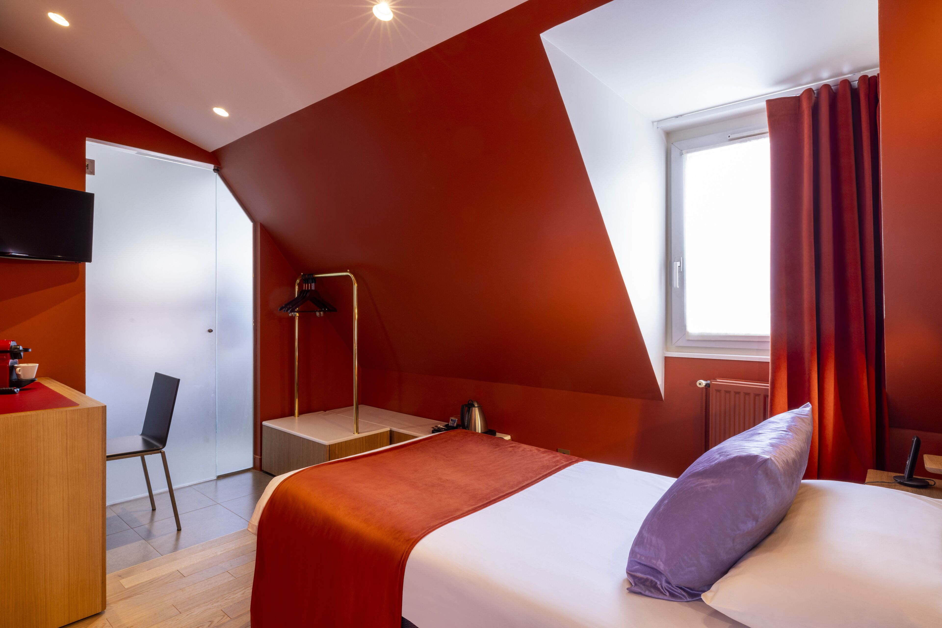 Una habitación de hotel moderna con una cama, un escritorio, una silla y un televisor fijado a la pared.