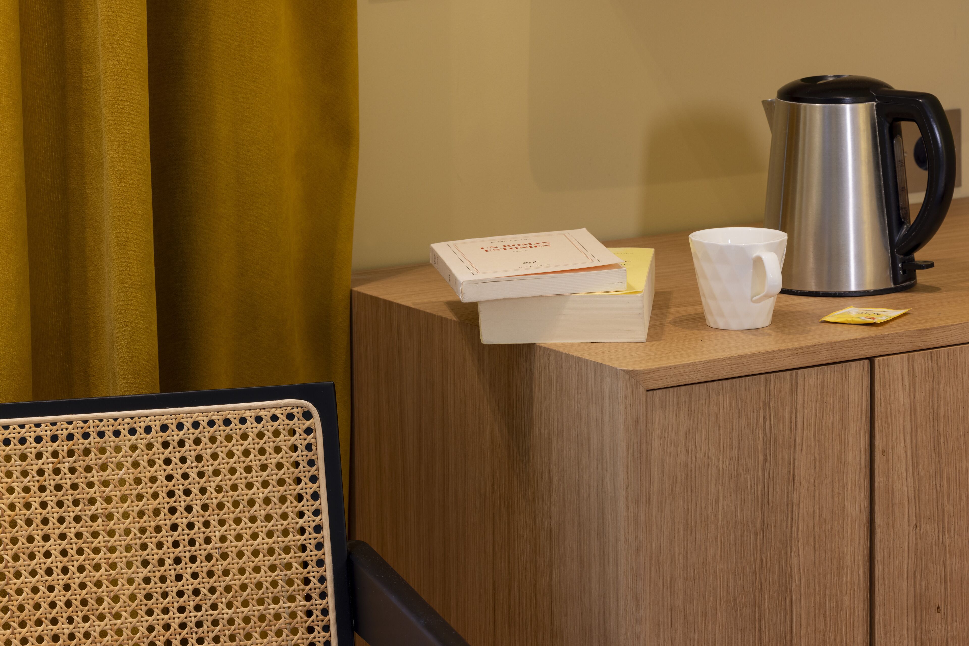 A wooden counter with a book, a white mug, and a stainless steel coffee pot.