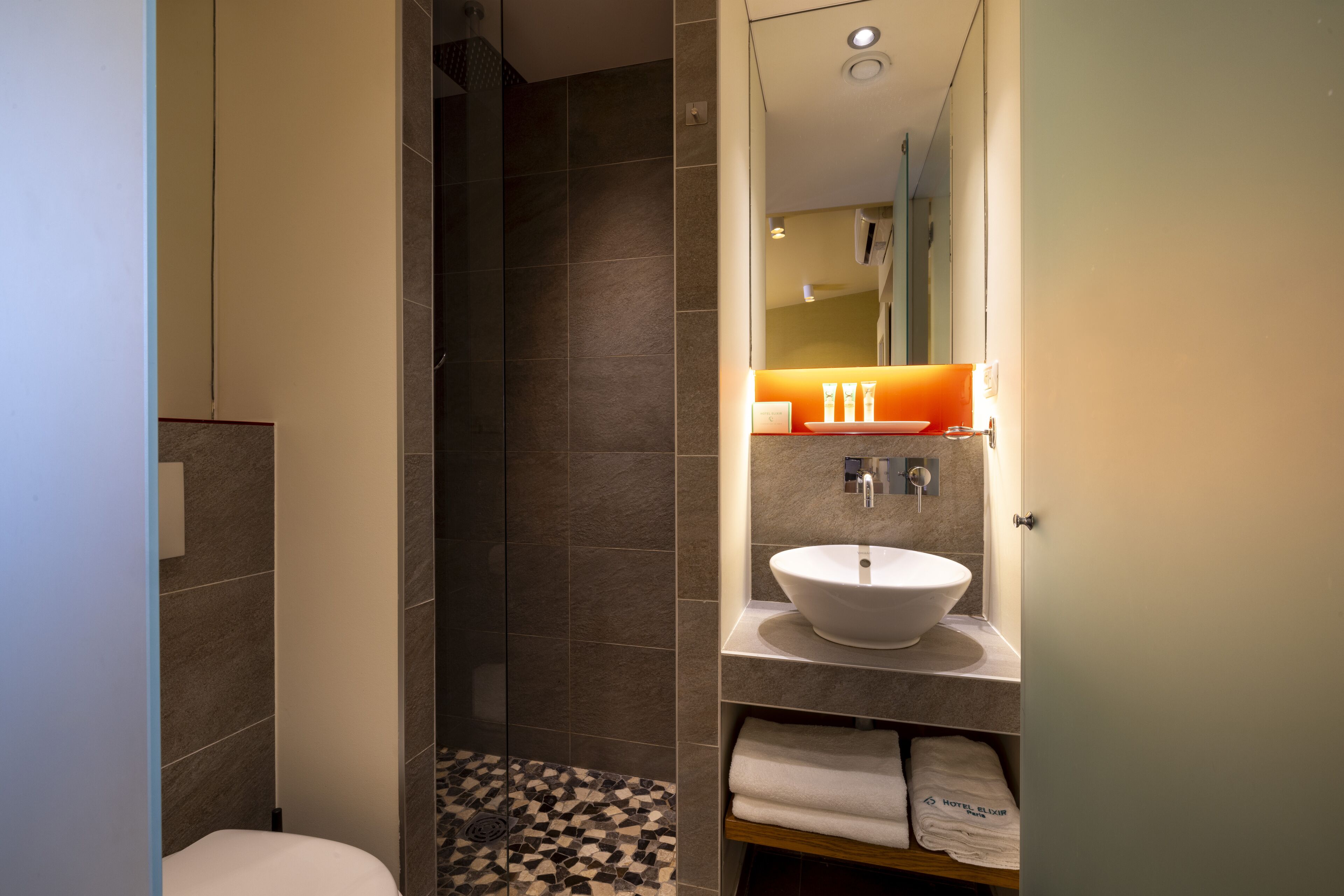 A modern bathroom with a large white sink, a mirror above it, and a shower area with a tiled floor.