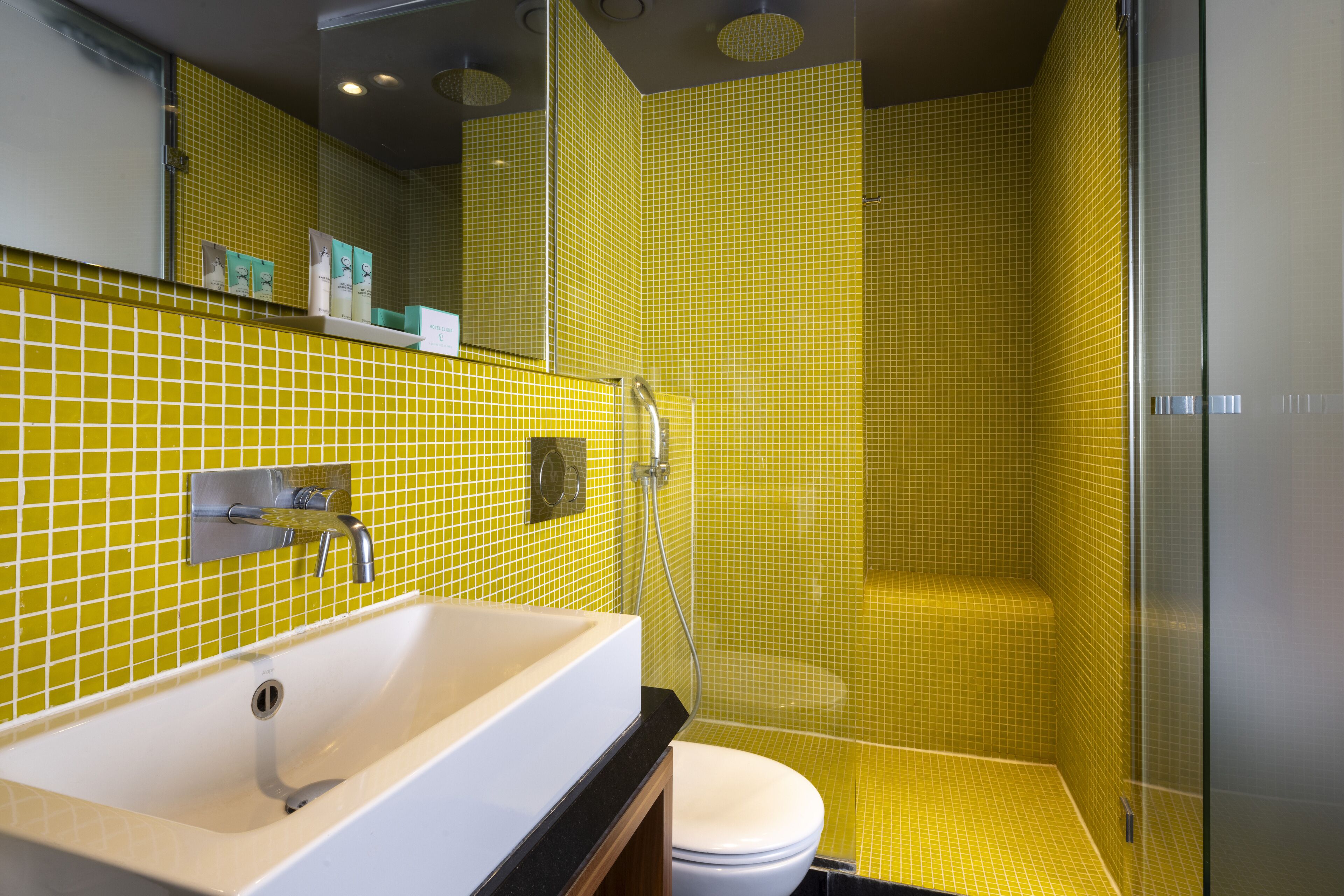 A bathroom with a yellow-tiled shower, a white sink, and a toilet.