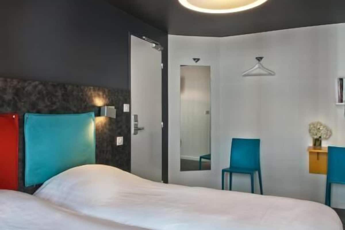 A modern hotel room with a bed, a mirror, a wardrobe, and a seating area.