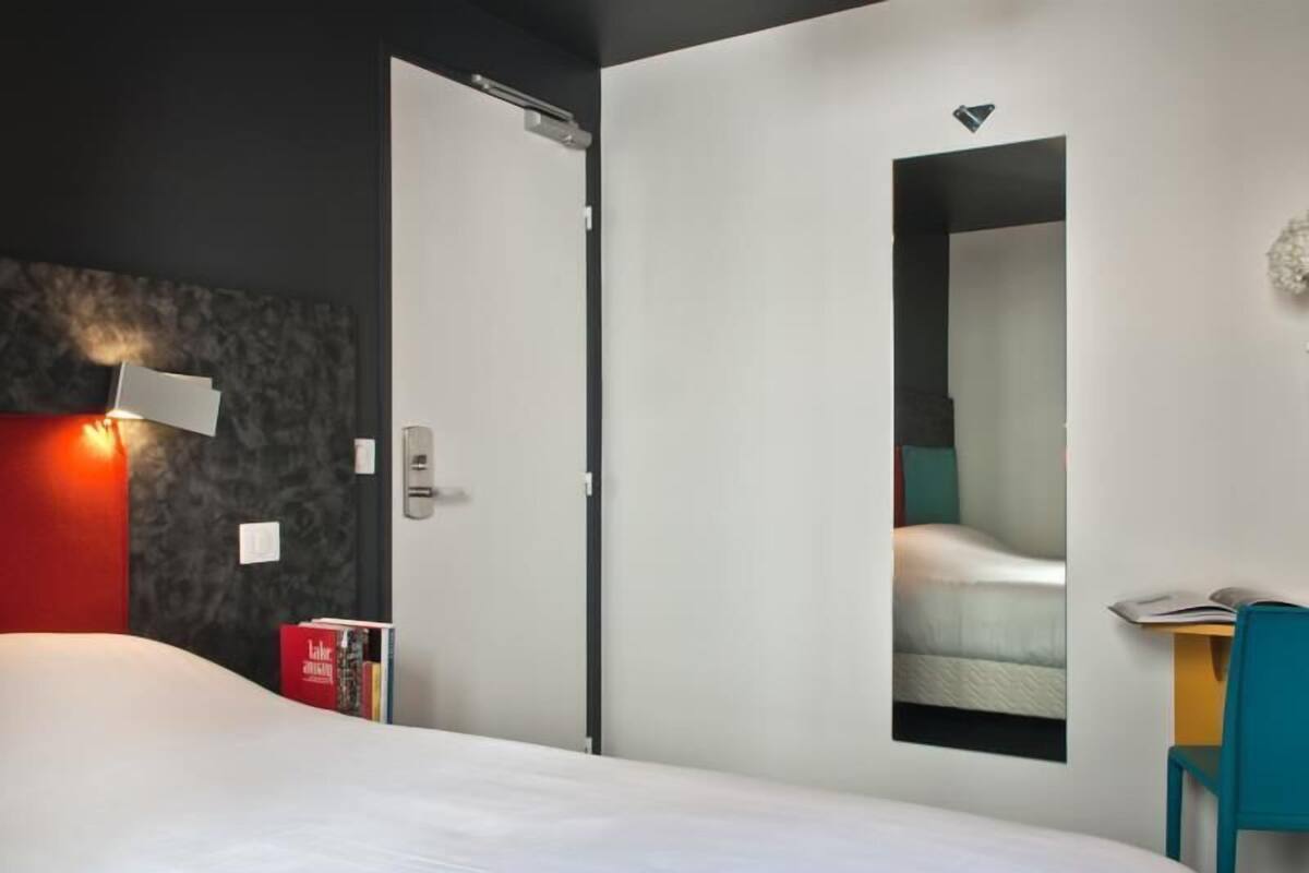 A modern hotel room with a bed, a desk, and a door with a mirror.