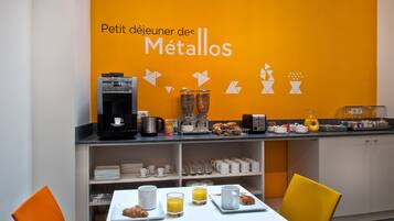 A breakfast area with a coffee machine, juice, croissants, and a buffet with various food items.