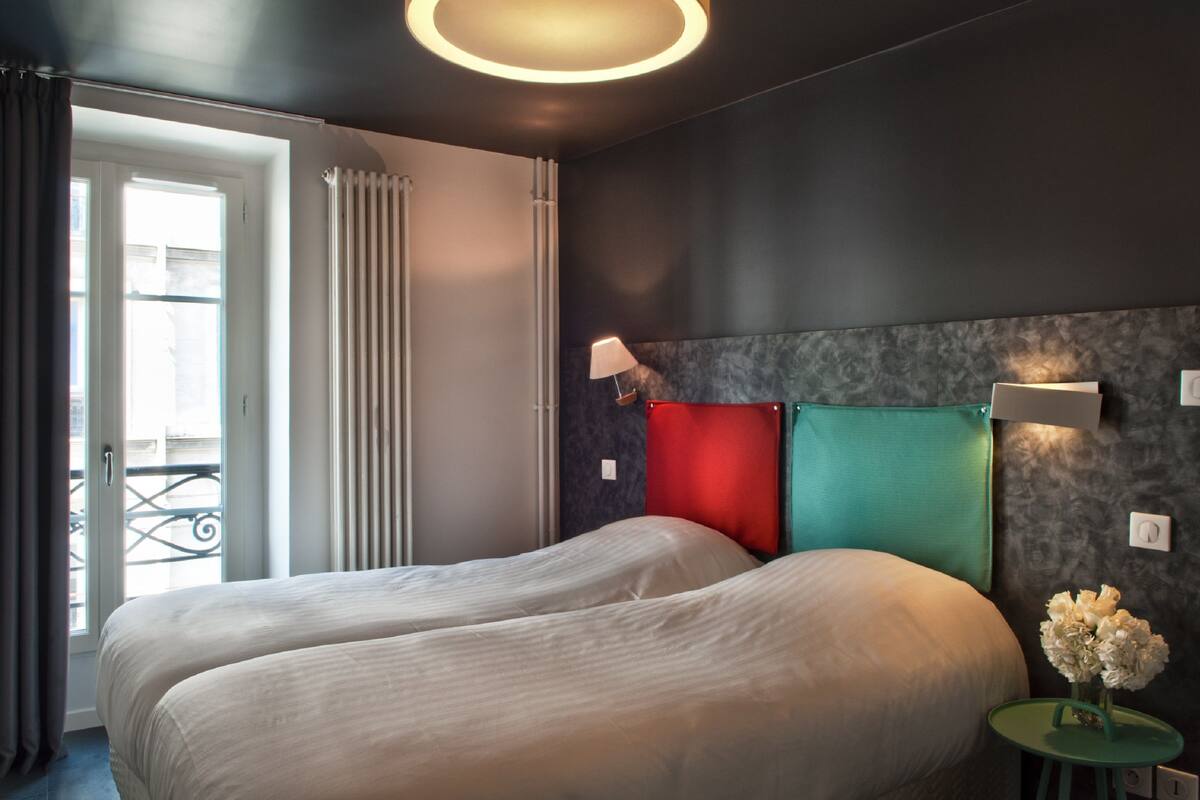 A hotel room with a bed, a nightstand, a lamp, and a view of the outside balcony.