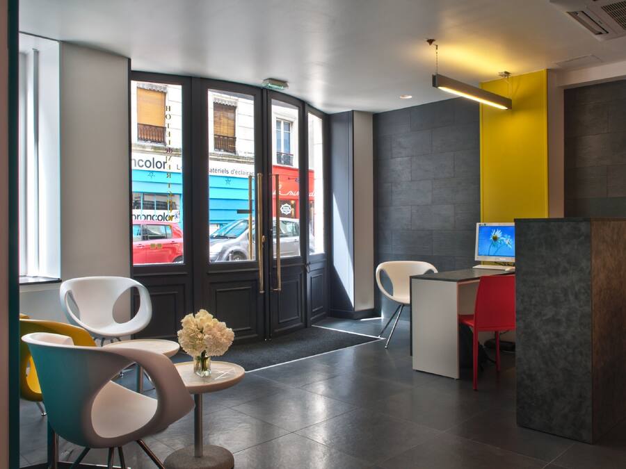 A modern hotel lobby with a reception desk, seating area, and large windows overlooking the street.