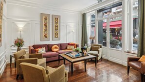 Un salon spacieux, comprenant un ensemble de canapés, une table basse et donnant sur la rue grâce à de grandes fenêtres.