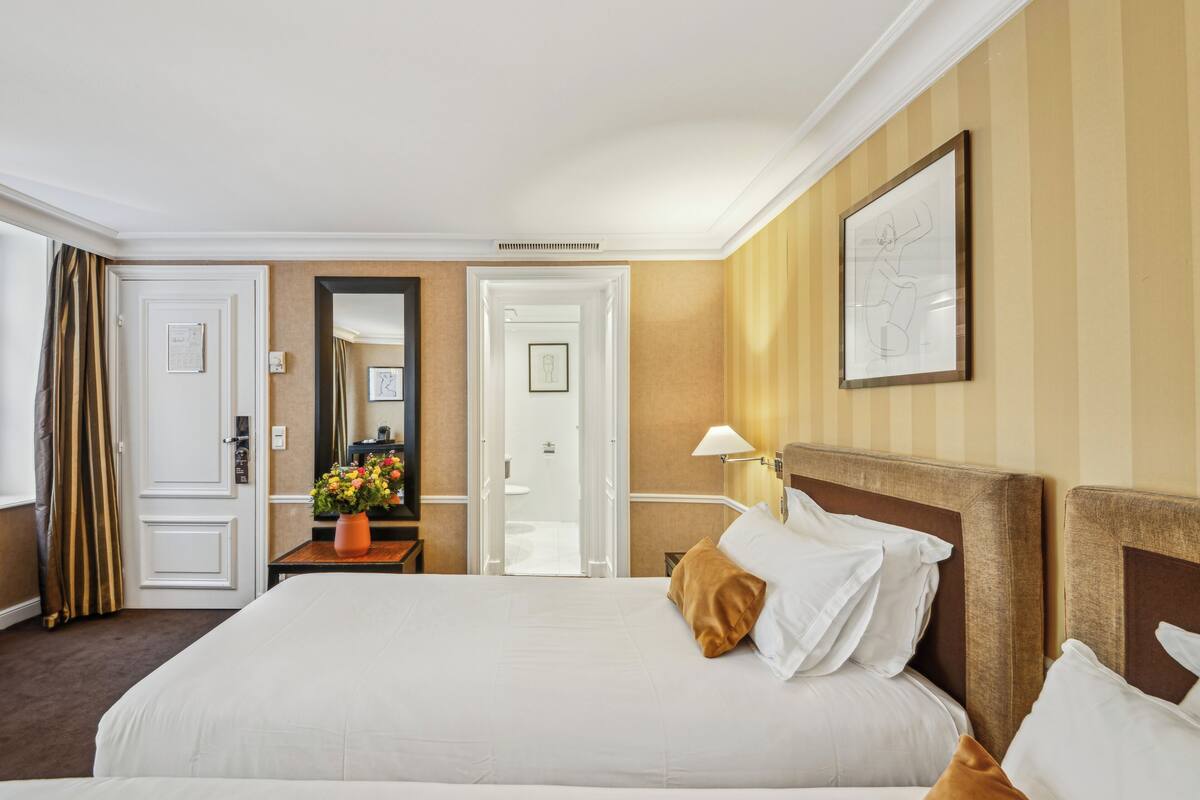 A hotel room with a large bed, a bedside table with a vase of flowers, a mirror, and a framed picture on the wall.