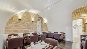 Un restaurant aux murs de pierre, aux tables dressées avec de la vaisselle blanche et aux chaises violettes.
