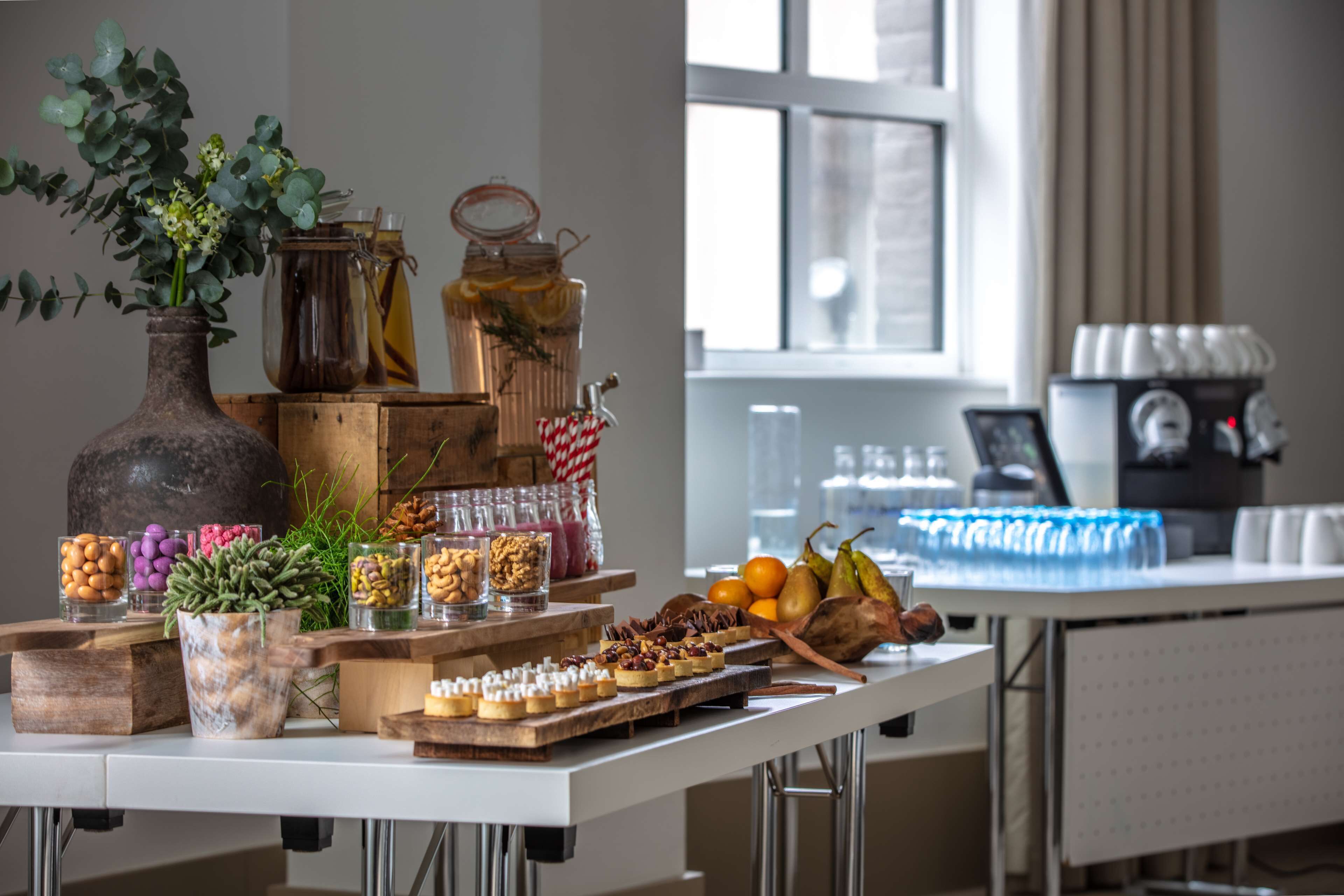 A buffet table with various food items, jars of nuts and fruits, and a vase with green plants.
