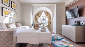 Habitación de hotel con cama, sofá, televisión, cafetera y vista a un paisaje urbano.