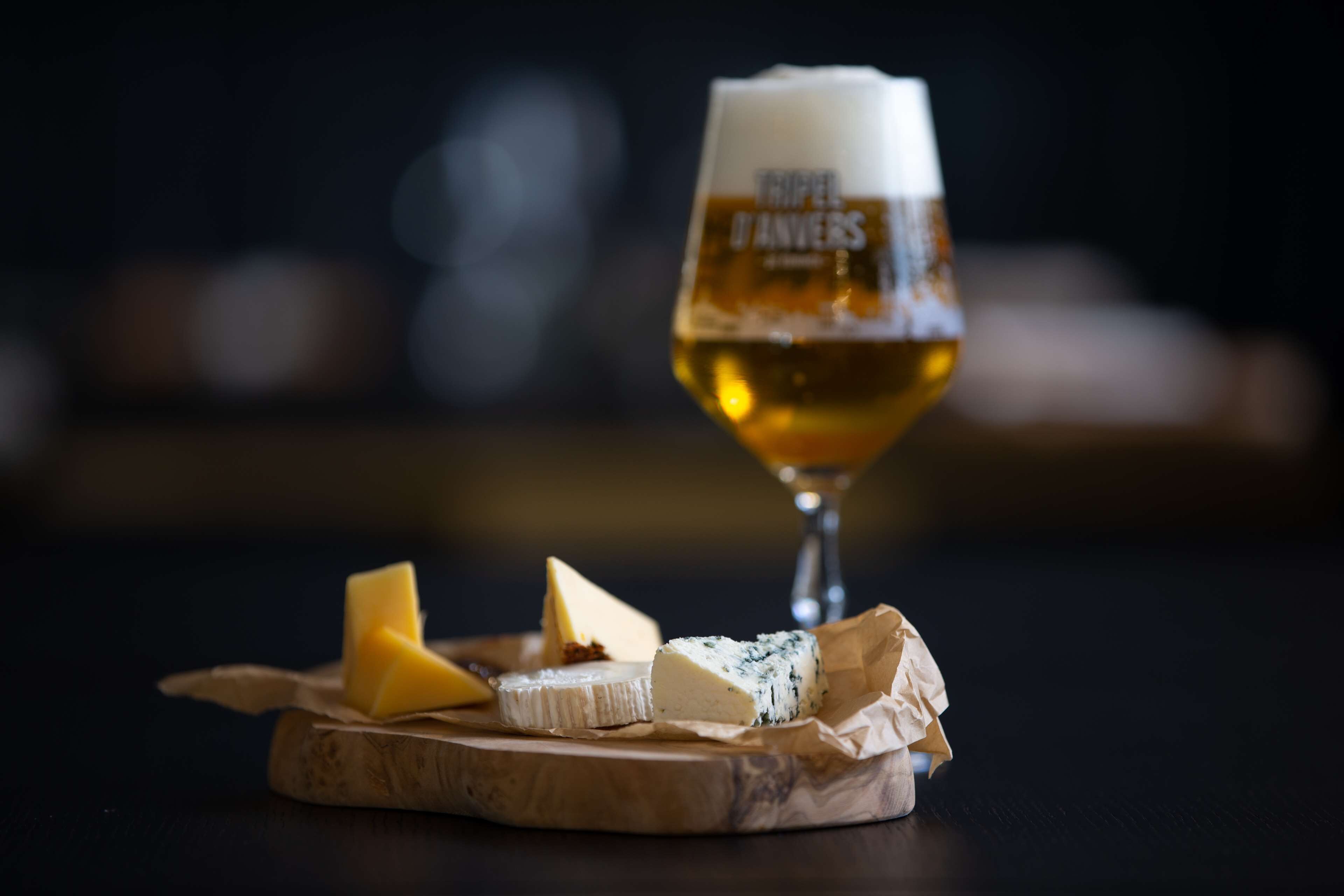 A wooden board with various cheeses and a glass of beer.