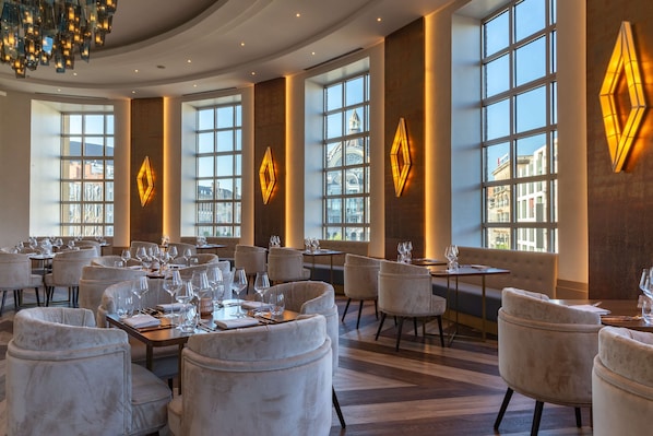 Un vaste espace dédié à la restauration dans l’hôtel, doté de grandes fenêtres, d’un mobilier élégant et d’un lustre.