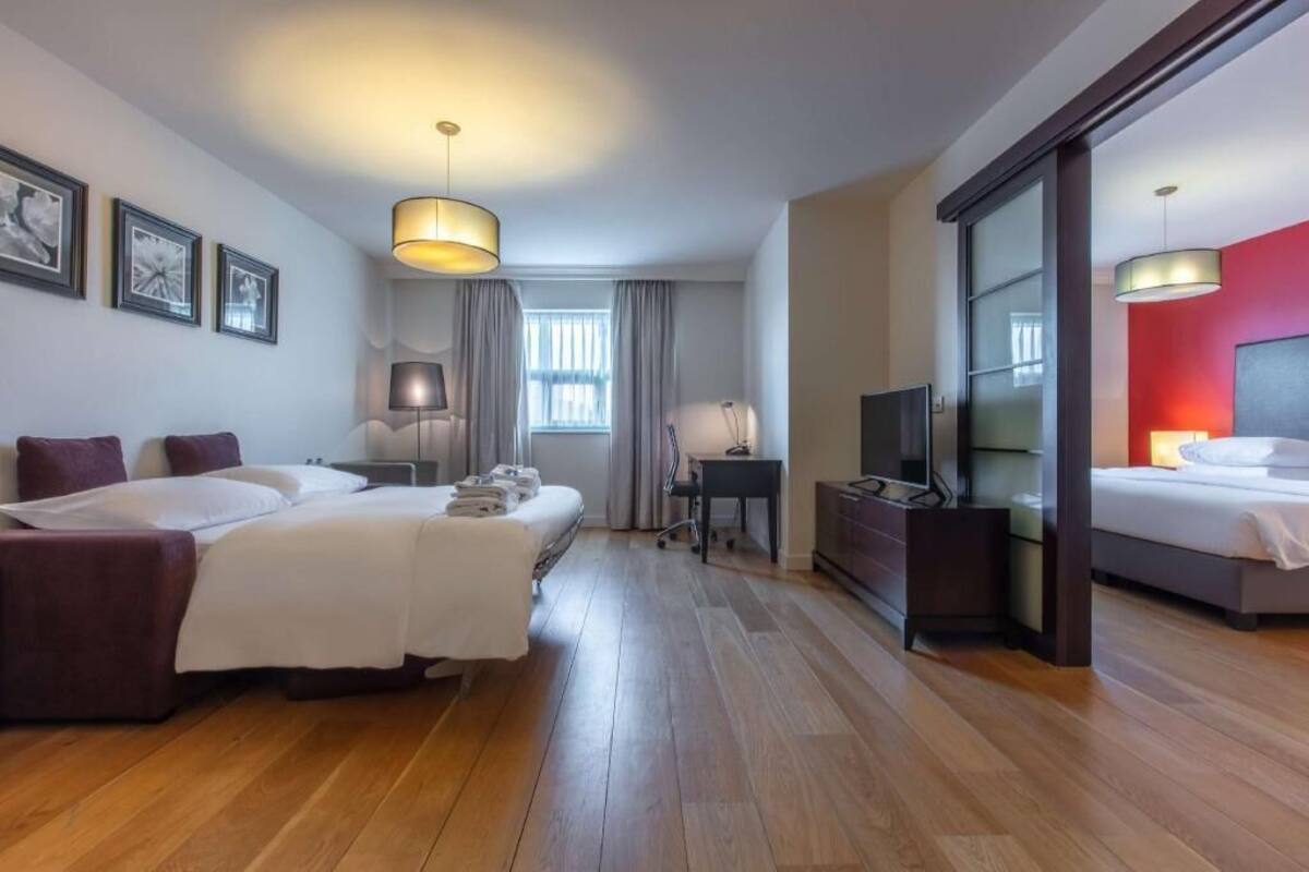 Habitación de hotel con dos camas, un escritorio, televisión y puerta corrediza a un balcón.