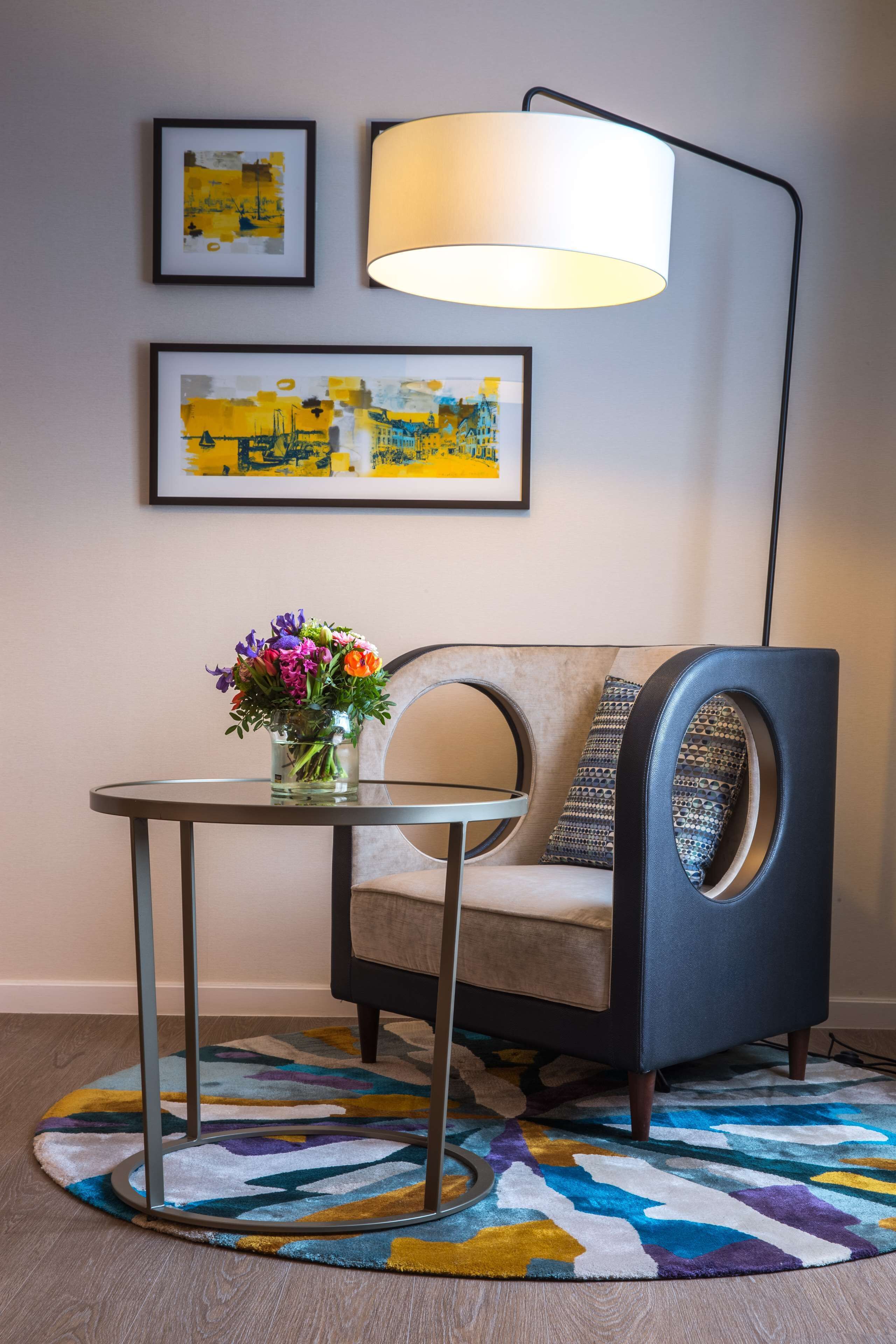 Une pièce moderne avec une table ronde, une chaise dotée d’un dossier circulaire original, un lampadaire et deux œuvres d’art encadrées accrochées au mur.