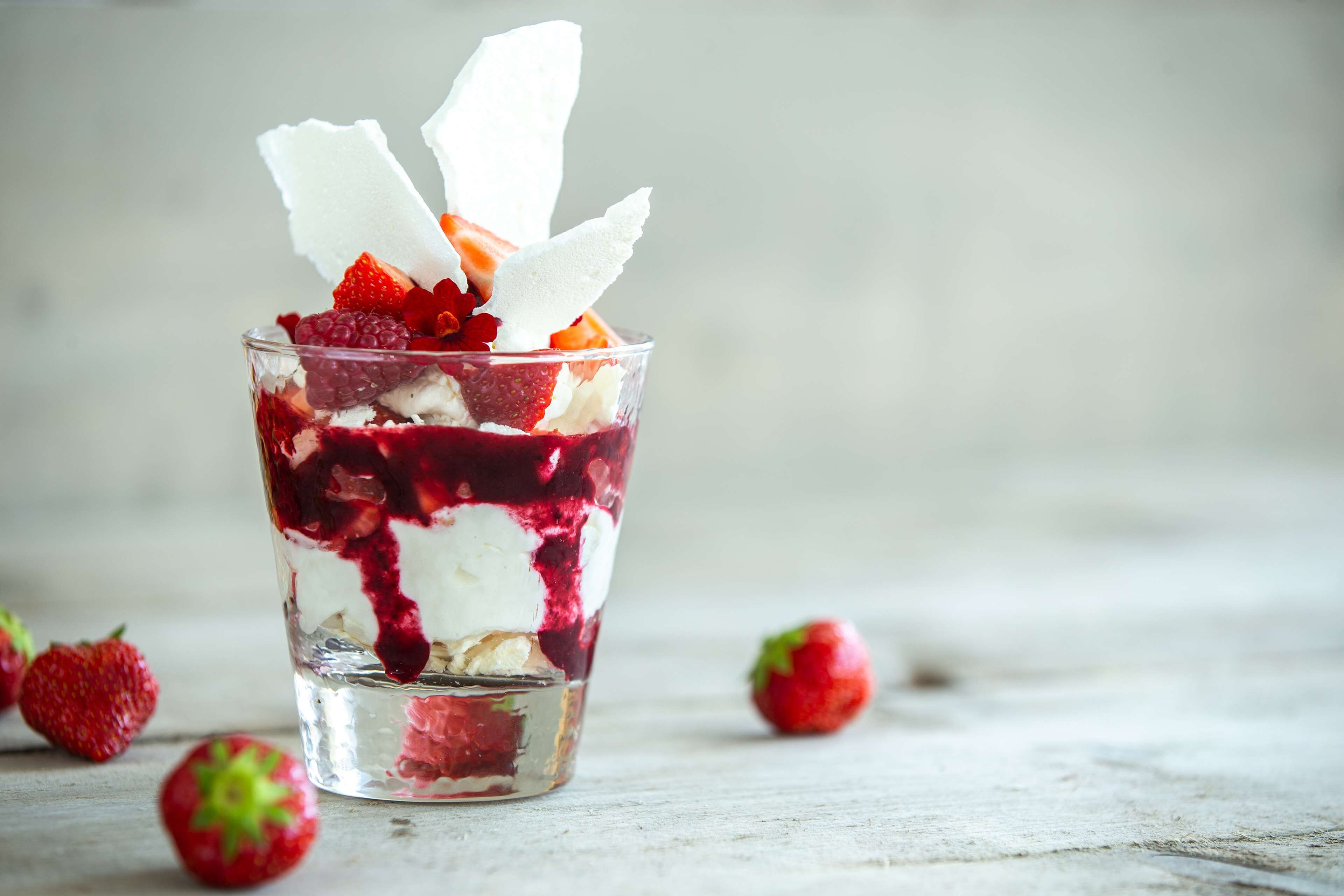 Un vaso transparente con un postre en capas de fresas y crema.